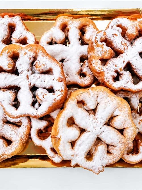 Flores de masa frita espolvoreadas con azúcar glas sobre una bandeja dorada, dulce tradicional de Dulces Caprichos en As Pontes