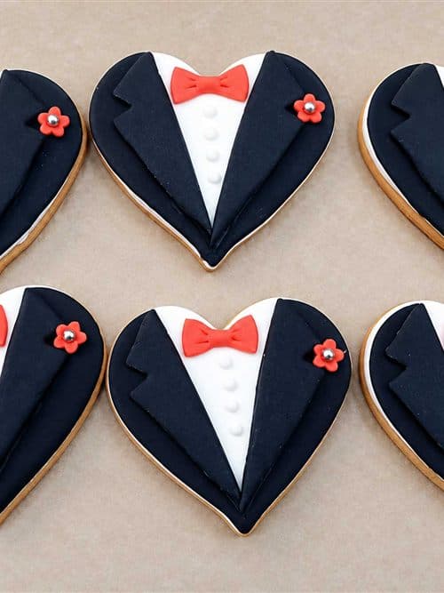 Galletas con forma de corazón decoradas como esmoquin con pajarita roja, elaboradas en la pastelería Dulces Caprichos de As Pontes